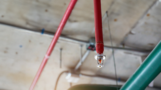 Närbild på ett sprinklersystem monterat i taket, med röda rör och en sprinklerhuvud i fokus.