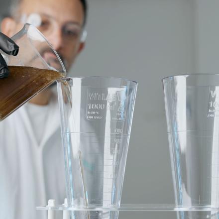 En specialist inom vattenrening, häller smutsigt vatten från en bägare i ett mätglas i en laboratoriemiljö.