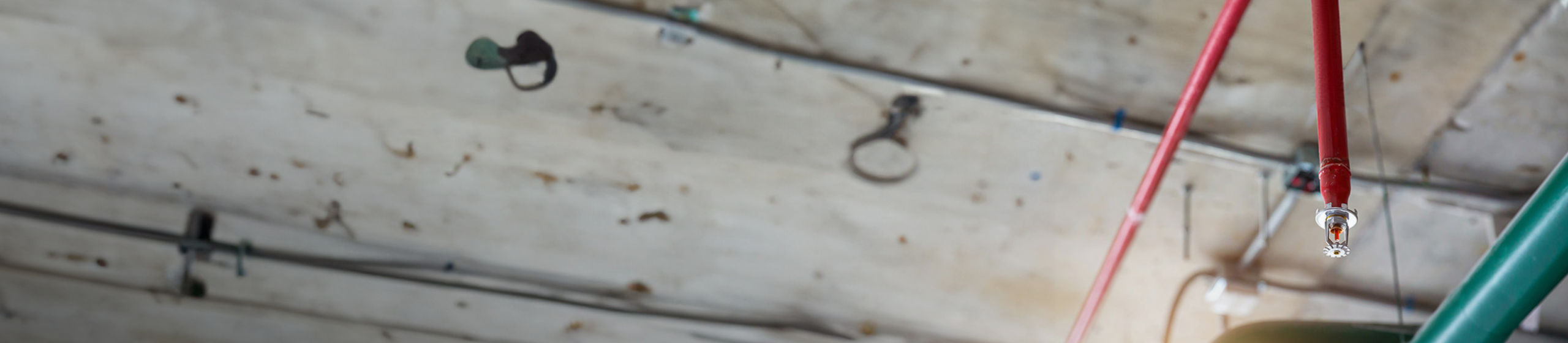 Närbild på ett sprinklersystem monterat i taket, med röda rör och en sprinklerhuvud i fokus.